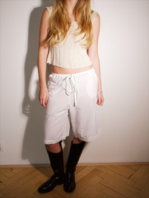 Model wearing the Fløre Barga pants, wide-leg cropped cotton pants with lace trim at the hem, paired with a knit tank