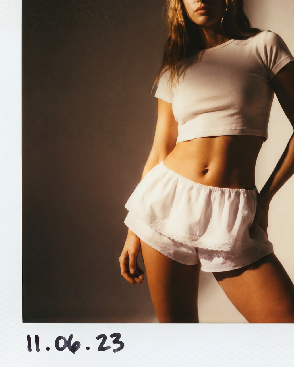 Polaroid-style photo of a person wearing a white top and shorts against a plain background.